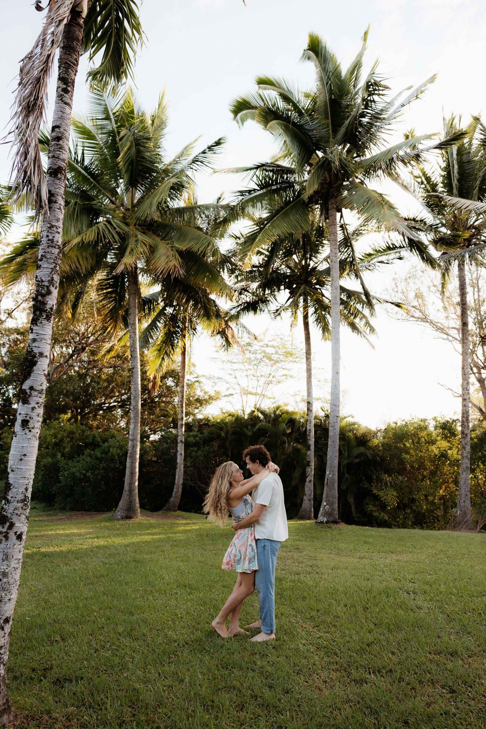 Engagement photo of a man and woman holding each other surrounded by coconut trees and palm trees.