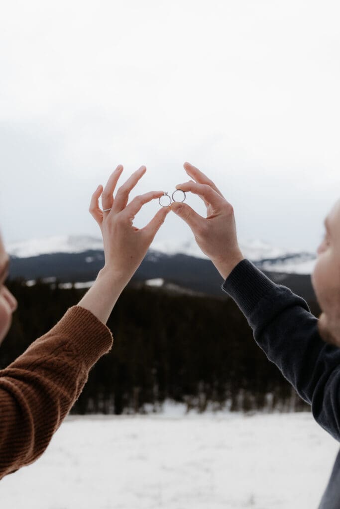 Photograph of engagement session in the Big Horn Mountains where the couple are holding up their rings to the sky.