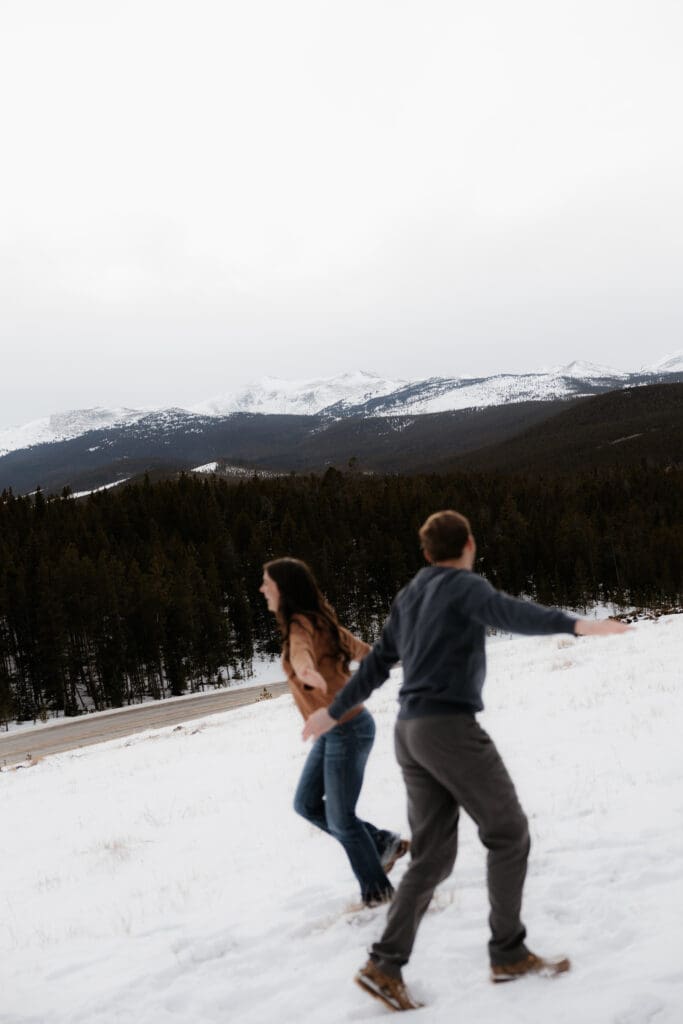 Photograph of engagement session in the Big Horn Mountains where the couple are making airplane motions and running around.