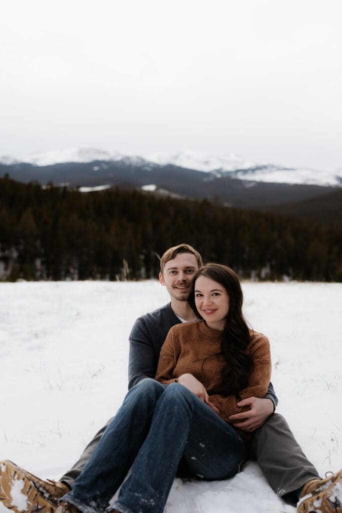 Photograph of engagement session in the Big Horn Mountains where the couple are sitting on the ground, smiling at the camera, with the woman between the mans legs.