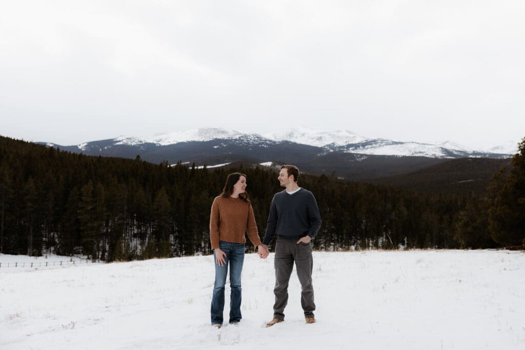 Photograph of engagement session in the Big Horn Mountains where the couple are standing side by side, holding hands, and looking at each other.