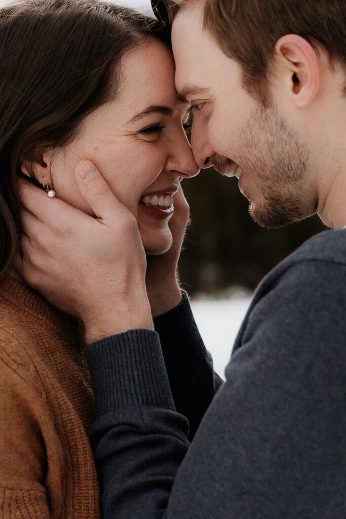Photograph of engagement session in the Big Horn Mountains where the man is holding the face of the woman and they are smiling at each other.