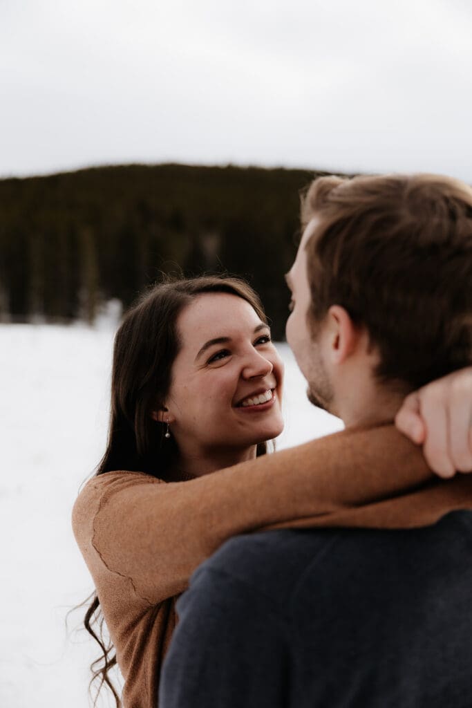 Photograph of engagement session in the Big Horn Mountains where the woman has her arms wrapped our the man and is smiling at him.