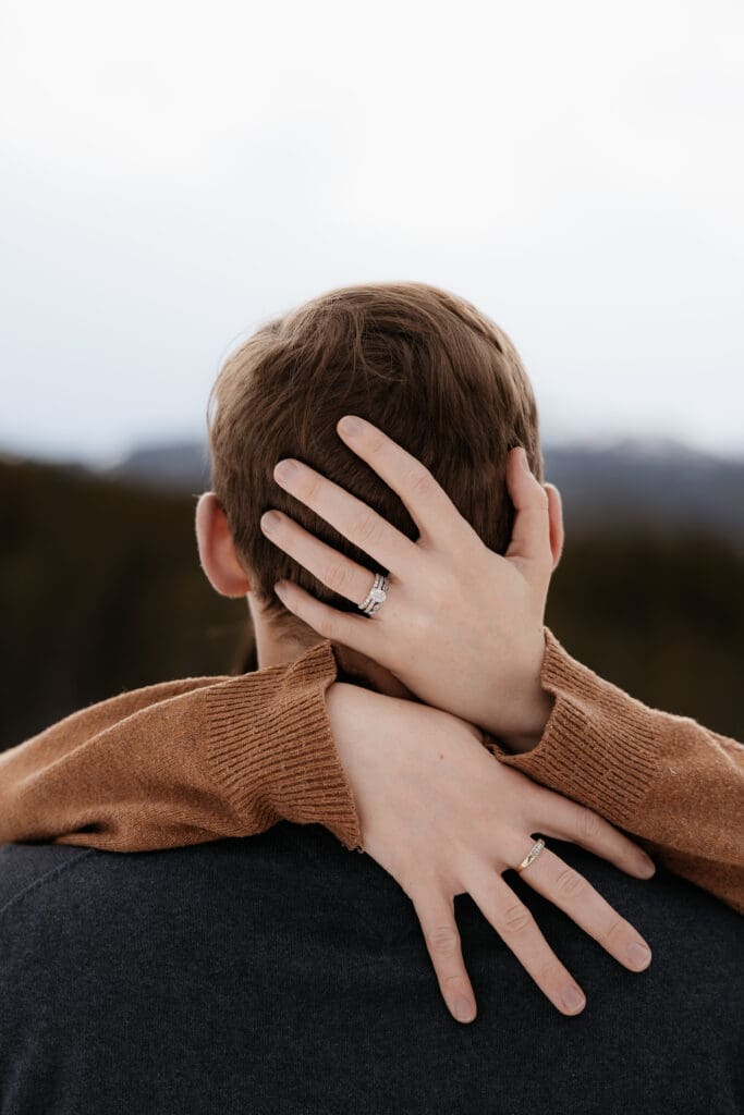 Photograph of engagement session in the Big Horn Mountains where the woman's hands are on the back of the mans head, showing off her ring.
