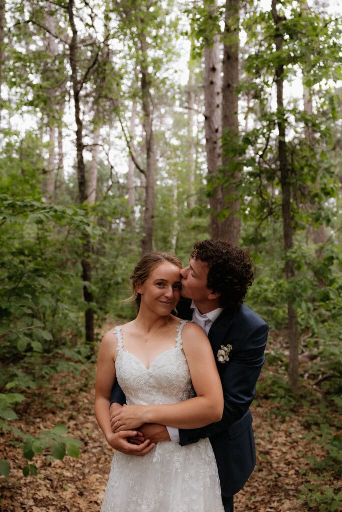 Wedding portrait of the groom holding the bride from behind and kissing her forhead.