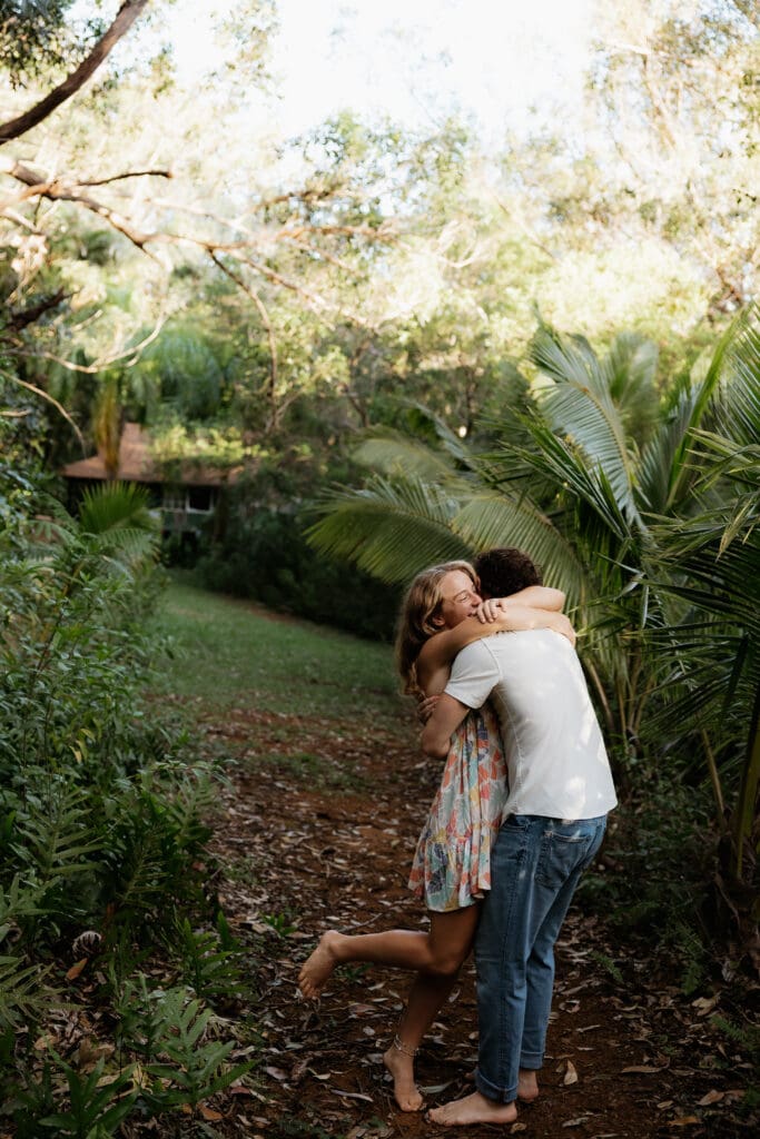 Engagement photo of man and woman embracing each other, surrounded by Hawaiian jungle foliage.