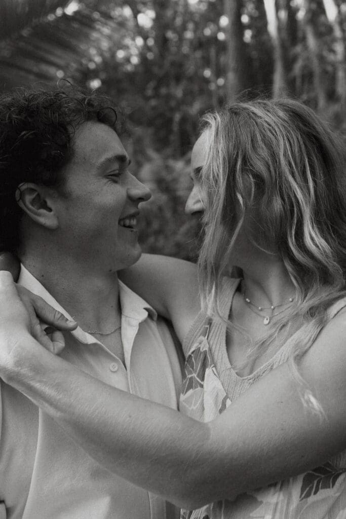 Black and white engagement photo of man carrying his woman while they laugh and smile.