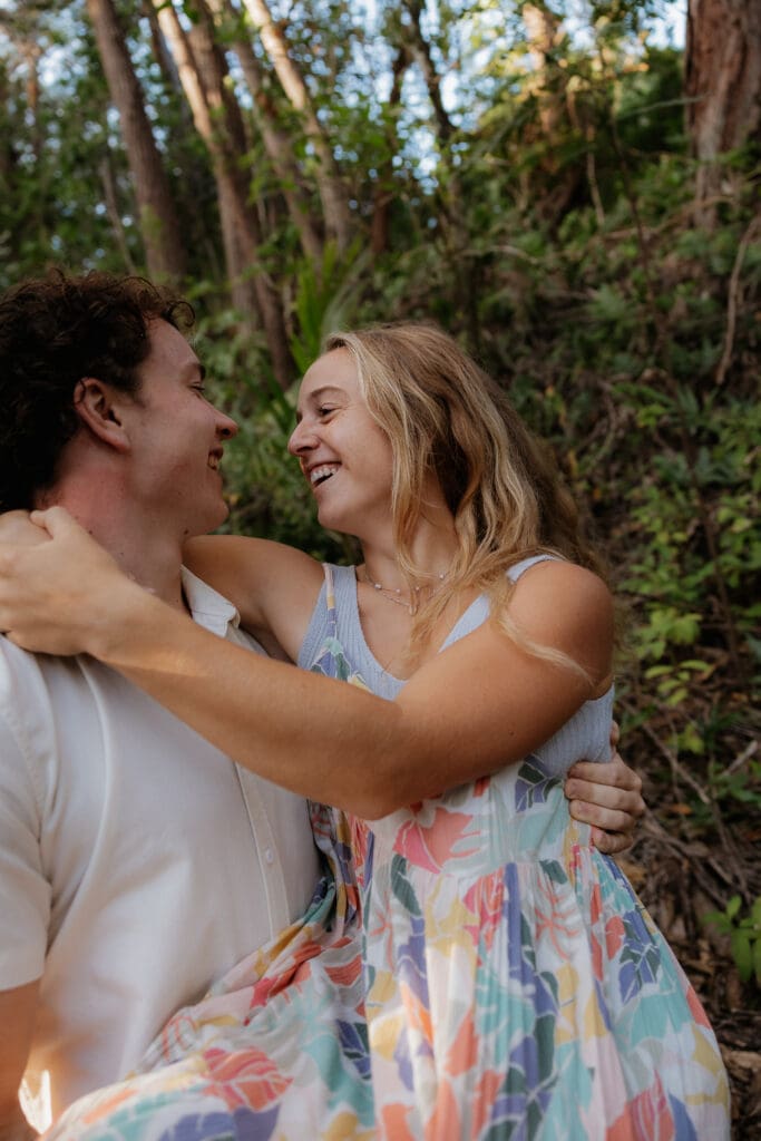 Engagement photo of man carrying his woman while they laugh and smile.