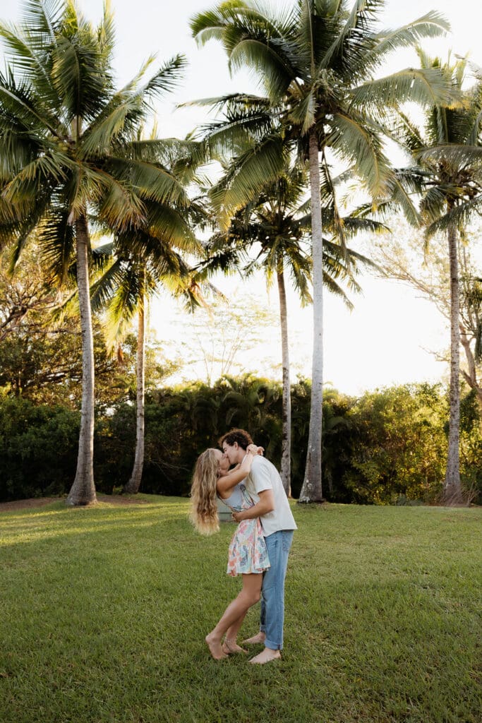 Engagement photo of man and woman facing each other and kissing, surrounded by coconut trees and palm trees.