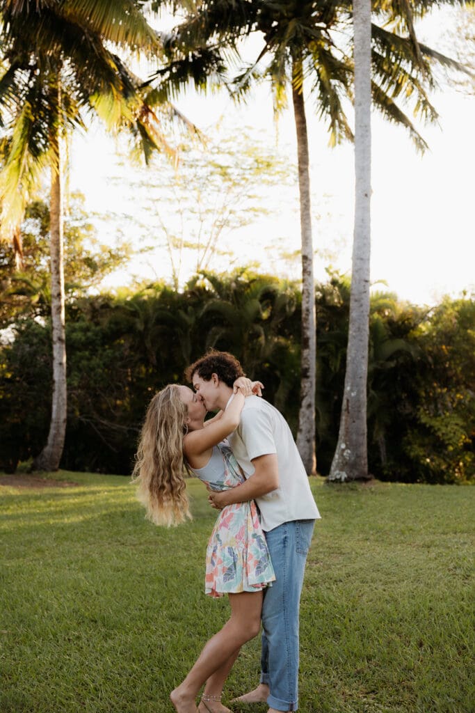 Engagement photo of man and woman facing each other and kissing, surrounded by coconut trees and palm trees.