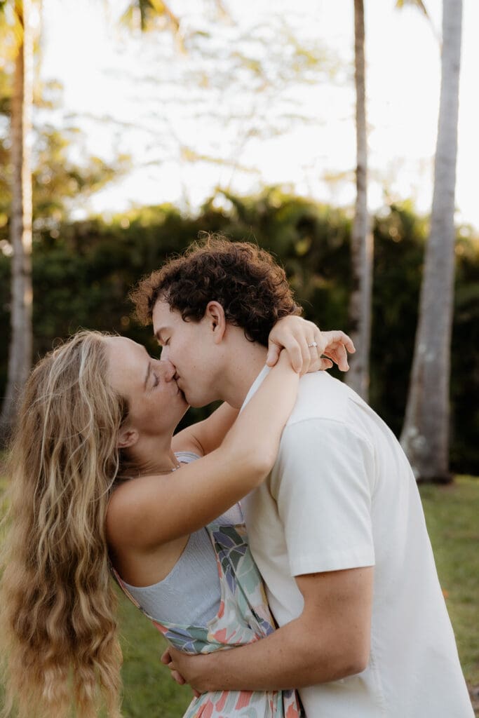 Engagement photo of man and woman facing each other and kissing, surrounded by coconut trees and palm trees.