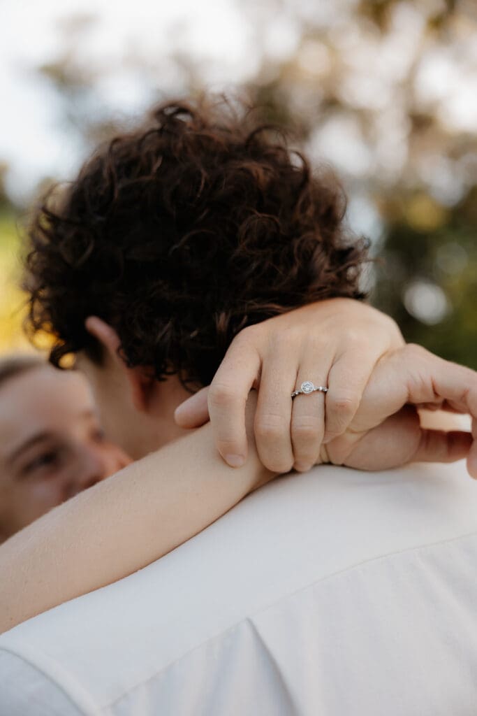 Engagement photo of the woman's ring as she has her arms wrapped around the mans neck.