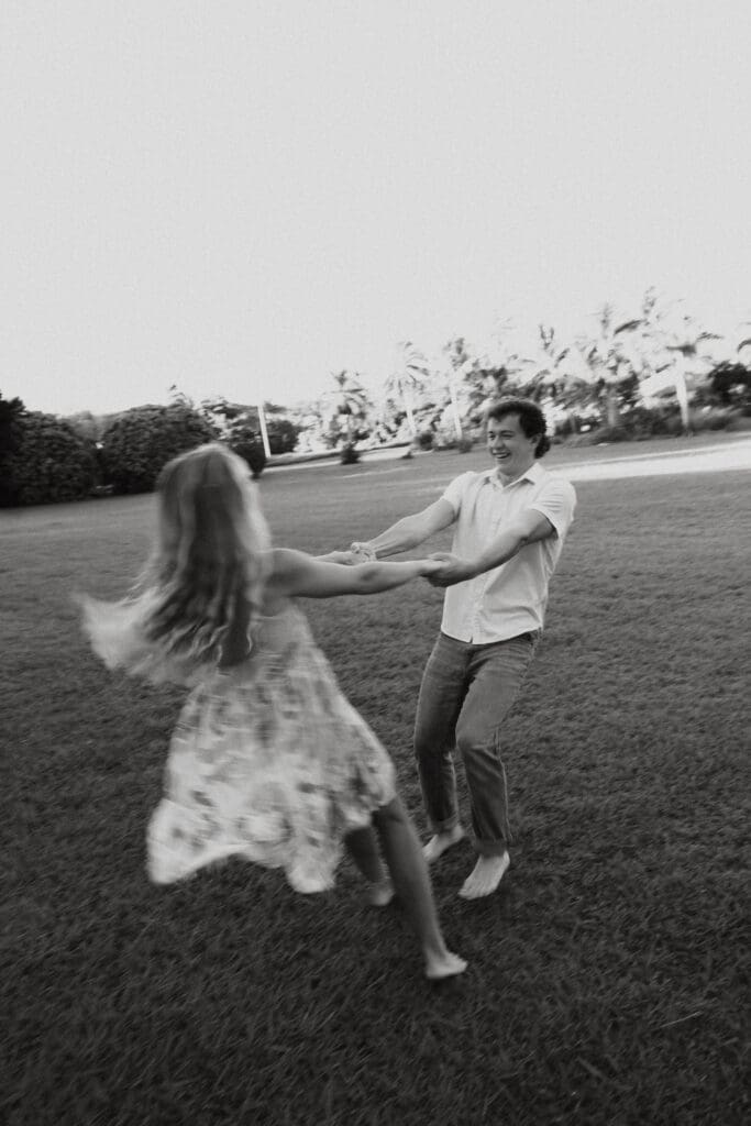 Black and white engagement photo of man and woman spinning around while holding hands and smiling.