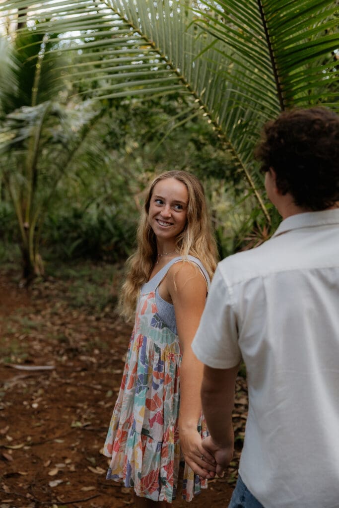 Engagement photo of woman leading her fiance and looking back at him while smiling.