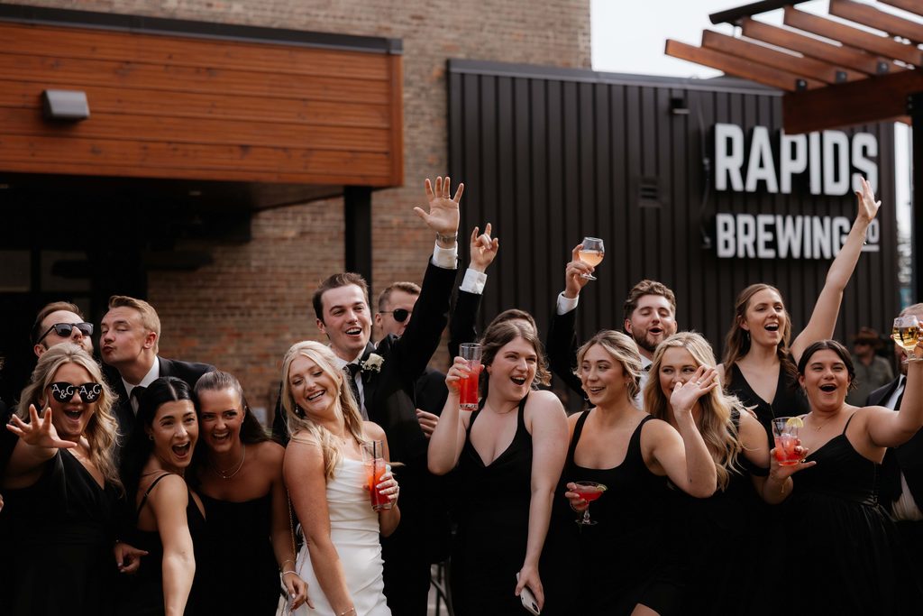 Wedding party looking at the camera and cheering as they celebrate their cocktail hour at a bar.