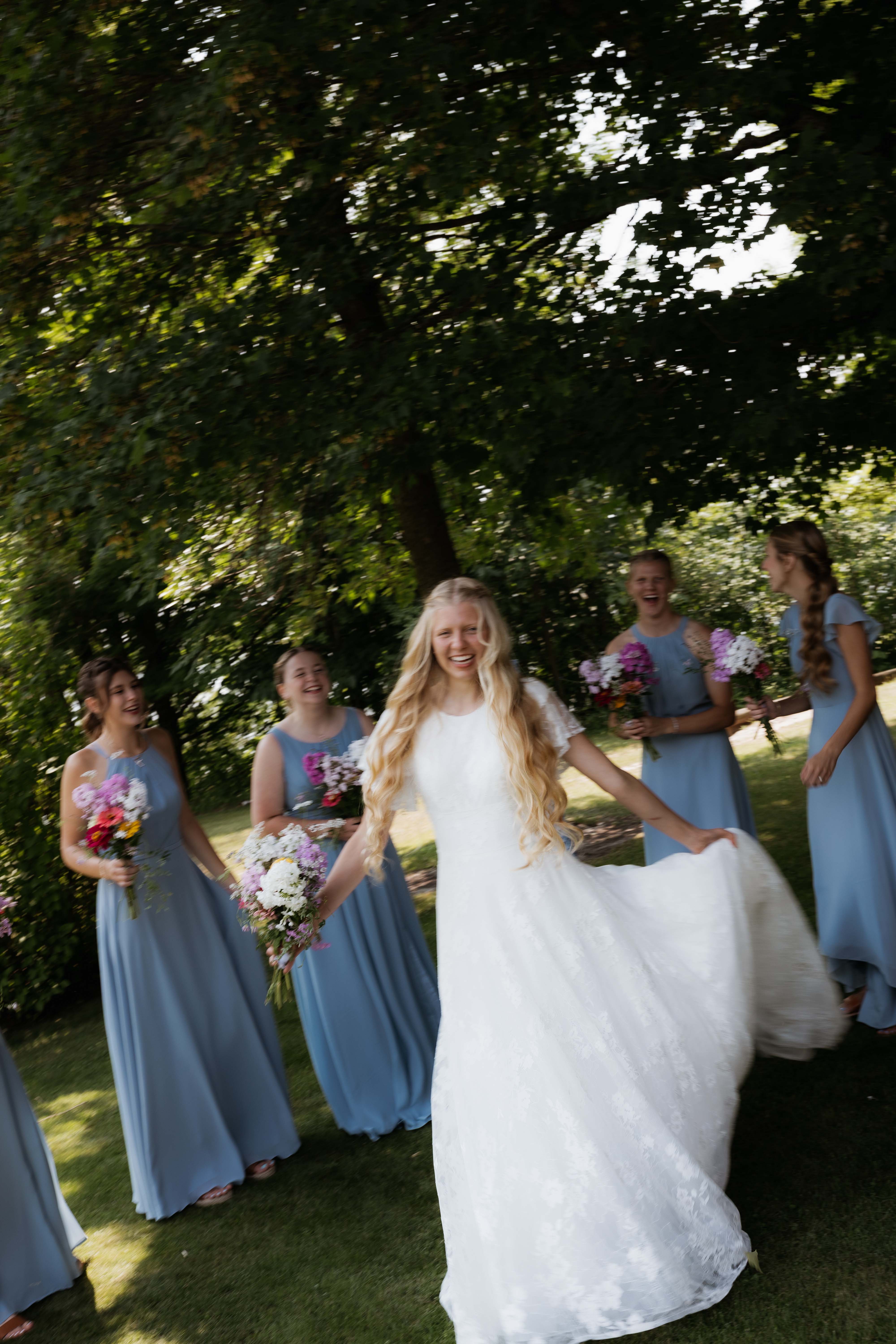 Bridal party surrounding the bride as she twirls around holding her dress and smiling.