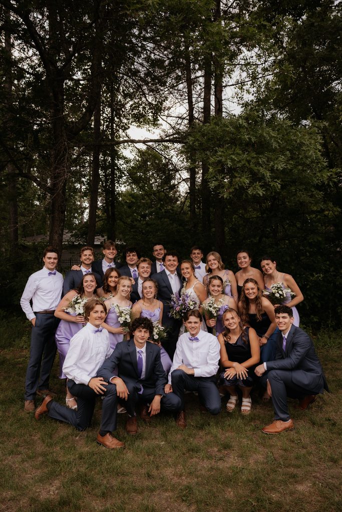 Wedding party surrounding the bride and groom as they smile at the caemra.
