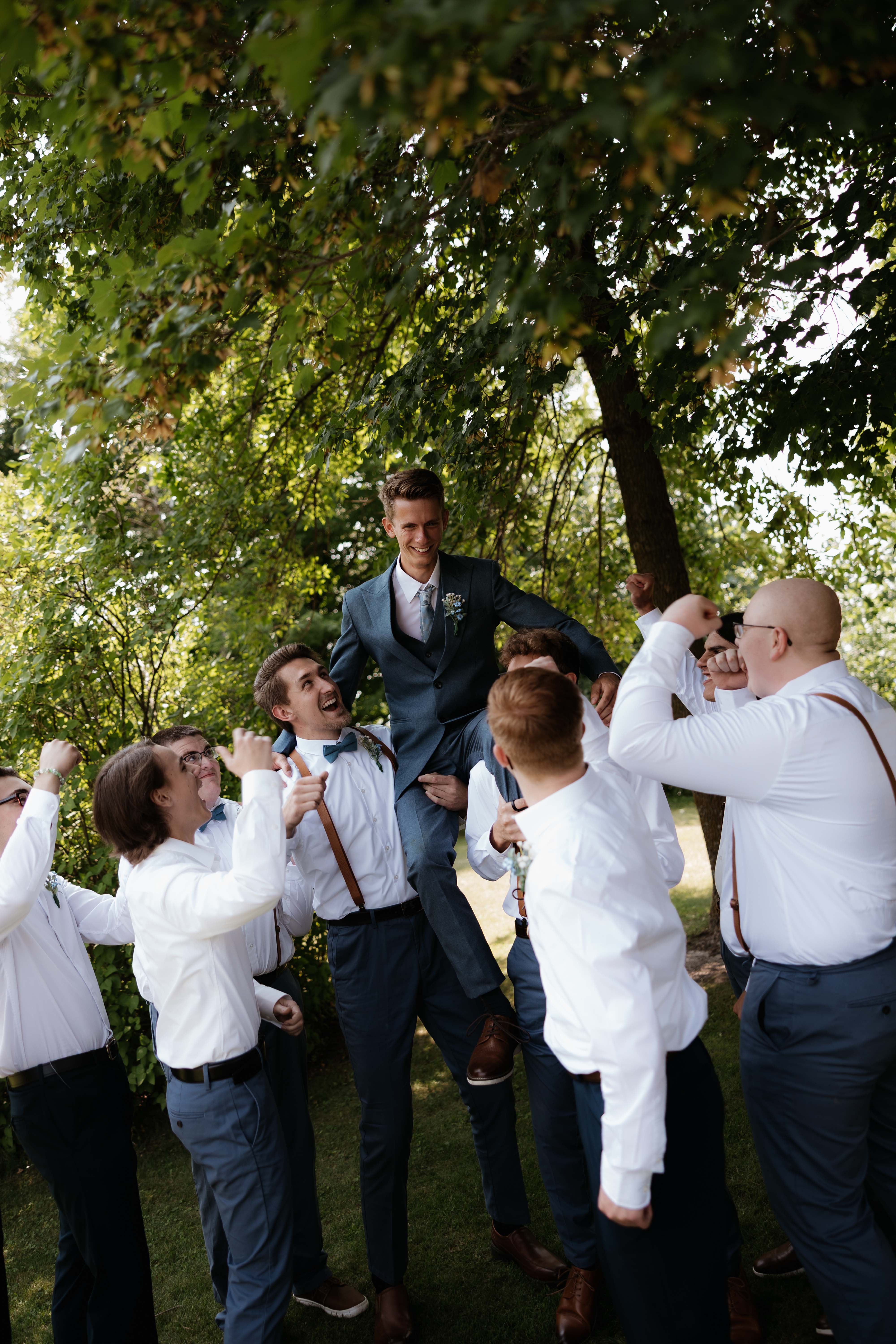 Groom on the groomsmens shoulders as they cheer him on.