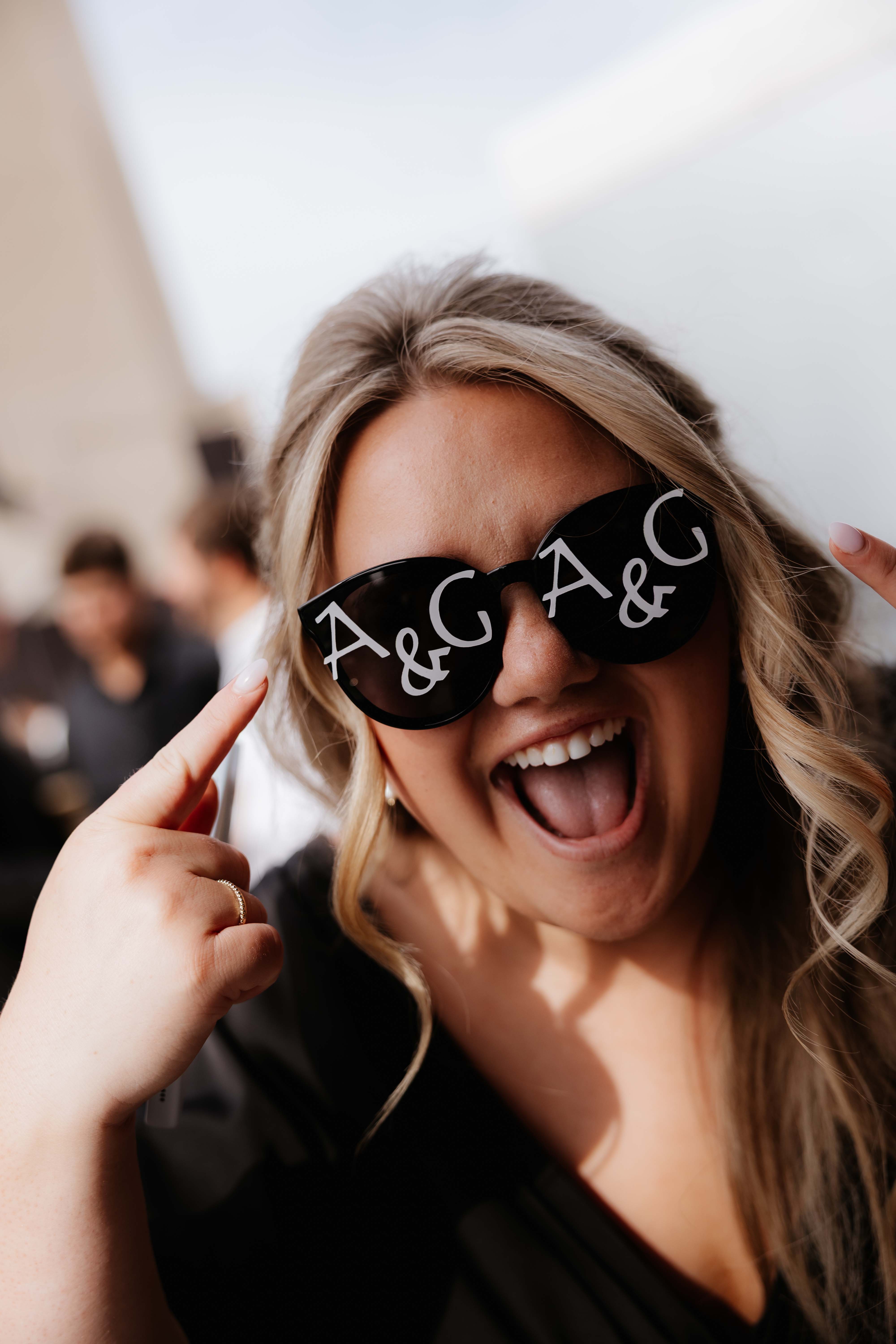 Bridesmaid wearing custom wedding glasses from the couple and pointing at the "A&G".